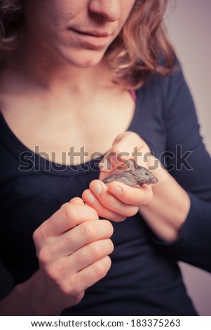 A young woman is holding her tiny pet mouse