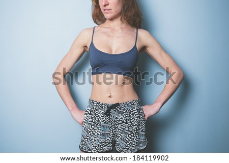 A young woman with toned abs is wearing sports clothing and standing against a blue background