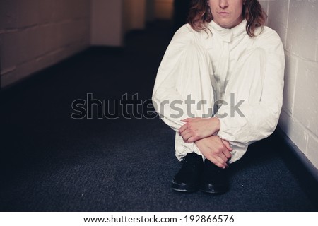A woman wearing a boiler suit is sitting in a corridor