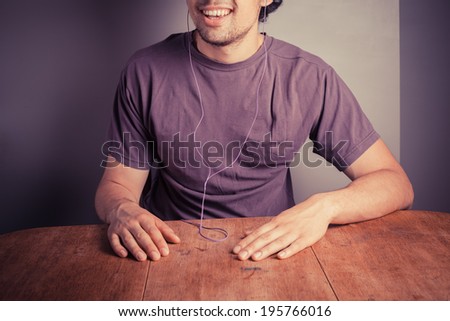 A young man is sitting at a table with earphones in his ears and is listening to music