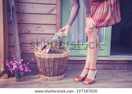 A young woman is standing on a porch with a basket of logs for firewood