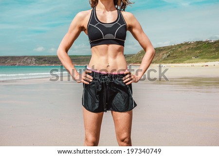 A fit young woman with toned abs is standing on the beach