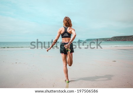 A young woman is standing and stretching her leg and back on the beach