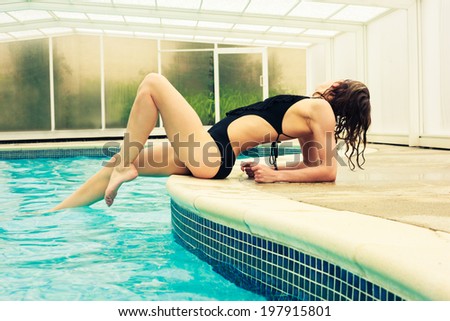 A sexy young woman in a swimsuit is posing by the edge of a swimming pool