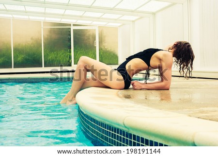 A sexy young woman in a swimsuit is posing by the edge of a swimming pool