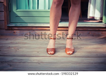 The naked legs of a young woman standing on a porch