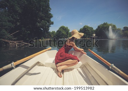 A young woman is sitting in a boat on the lake and is relaxing on a sunny day