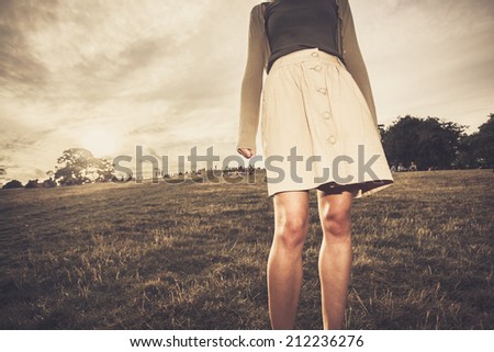 A young woman\'s skirt is blowing in the wind as she is standing in a park at sunset