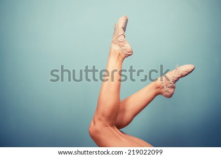Slender female legs wearing ballet slippers against blue background