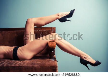 A sexy young woman wearing high heels is relaxing on a sofa in her underwear