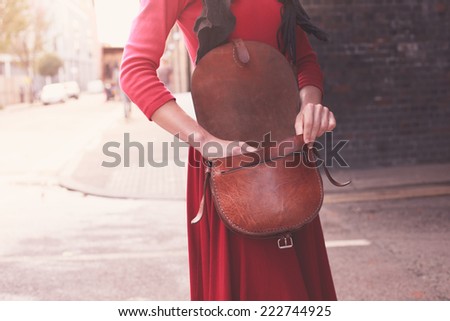 A young woman is standing in the street with her handbag open