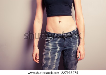 A young woman with toned abs is posing in front of a purple wall