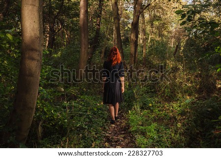 A young redhead woman is walking alone in the woods or enchanted forest