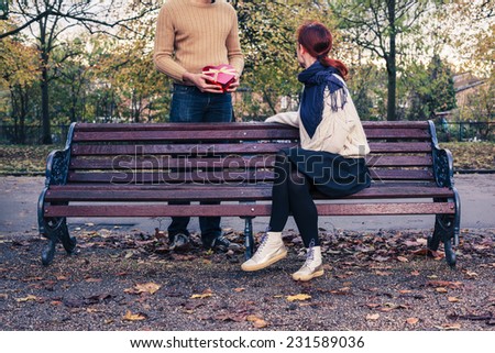 A young man is meeting a woman in the park and is giving her a lovely gift