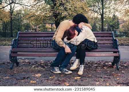 A sad young couple is embracing on a park bench in autumn