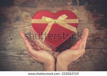 A man\'s hands are resting on a wooden surface with a heart shaped box
