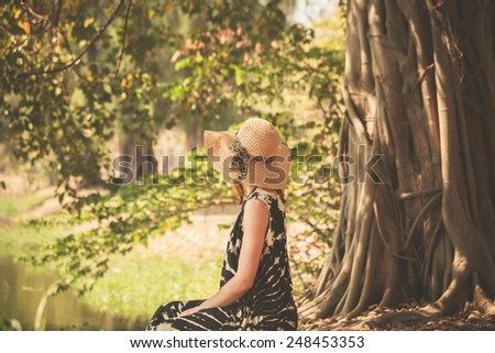 A young woman is sitting under a tree by the river