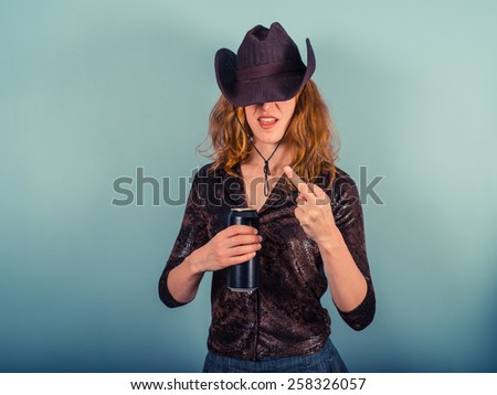 A young woman wearing a cowboy hat is drinking from a beer can and displaying rude gesture