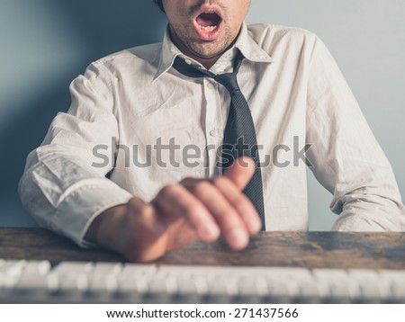 A young businessman is typing on a computer with one hand. His other hand is under the table and he is looking really excited.