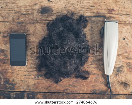 A smartphone, a pile of hair and some hair clippers on a wooden table