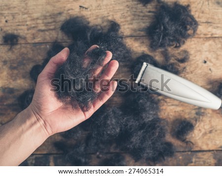 A male hand is holding some cut hair by a wooden table with a hair clipper