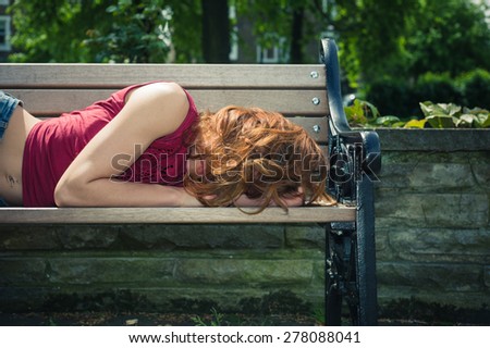 A young woman is lying down and relaxing on a park bench on a sunny  summer day