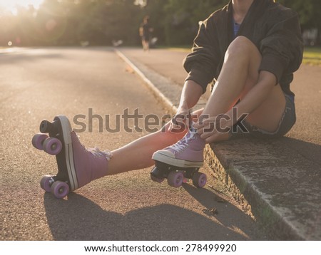 A young woman is sitting on the ground and is putting on roller skates in the park at sunset