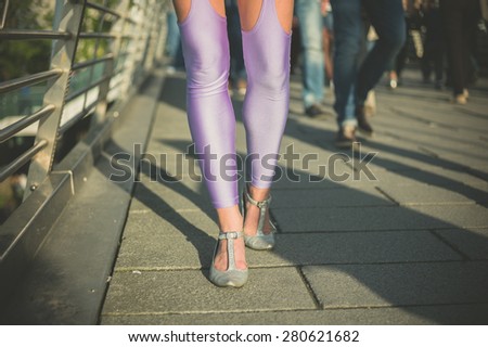 A young woman wearing heels and sexy leggings is walking on a pedestrian bridge in the city