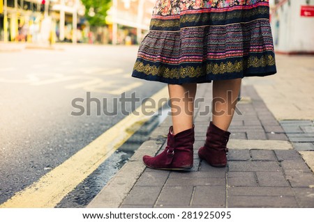 The legs of a young woman wearing a colorful skirt as she is standing in the street