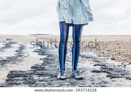 The legs of a young woman as she is standing on the beach with her skirt blowing in the wind