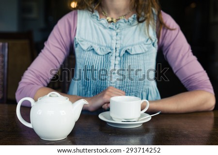 A young woman is having tea at a table in a dining room