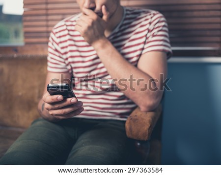 A young man is sitting on a sofa and is using a smart phone at home