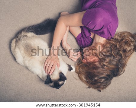 Overhead shot of a young woman lying on a carpet at home and petting a cat