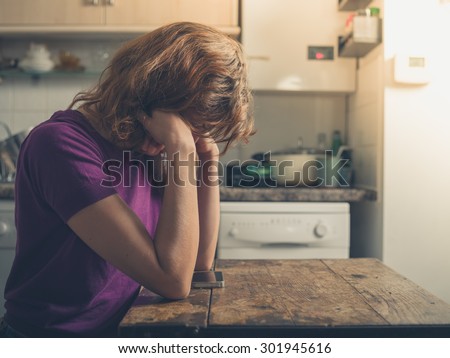 A young woman is using a smart phone at a table in a kitchen