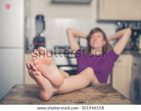 A young woman is relaxing in a kitchen with her bare feet on a table