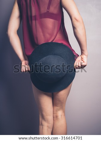 A young woman wearing seductive lingerie is holding a hat to cover up her behind