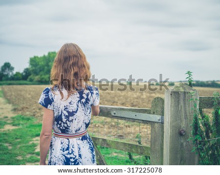 A young woman wearing a dress is opening a gate in the countryside on a gloomy and cloudy day