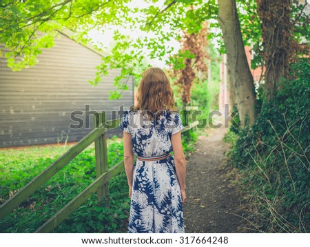 A young woman wearing a dress is standing on a footpath in a rural country setting