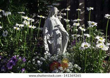 Statue of the Blessed Virgin Mother Mary in beautiful backyard flower garden.  Daisies, petunias, violas and roses surround her in a showy display of color.