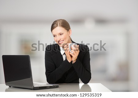 Smiling businesswoman sitting with laptop computer, holding coffee and tea mug