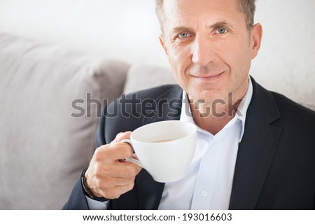 Happy mid age man in suit drinking coffee at home