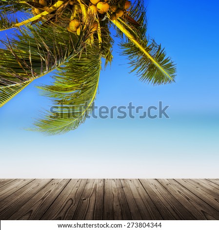Empty wooden table. Coconut palm trees, sandy beach, ocean and perfect sky. Tropical background.