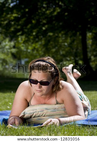 Beautiful woman laying on a blanket in a park reading a book.