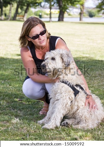 Woman sitting down, correcting a dog, outdoors in a park.