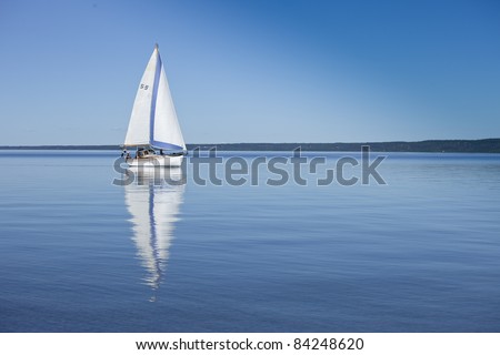 Boat reflecting in the water, sailing in calm, blue water. Swedish flag on boat
