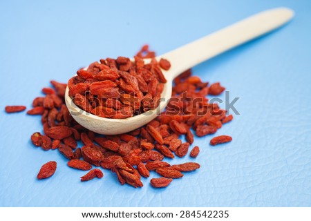 dried berries of a barberry in a wooden spoon on a blue background, selective focus