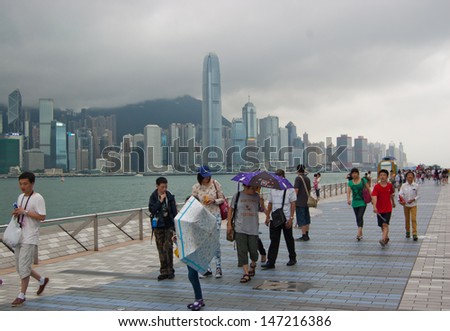 HONG KONG, CHINA, JUNE 24: Tourists walking along Avenue of Stars during monsoon season on June 24, 2013. In the background Victoria Harbor and skyscrapers on Hong Kong island.