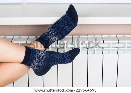 Woman's legs in socks on white radiator background
