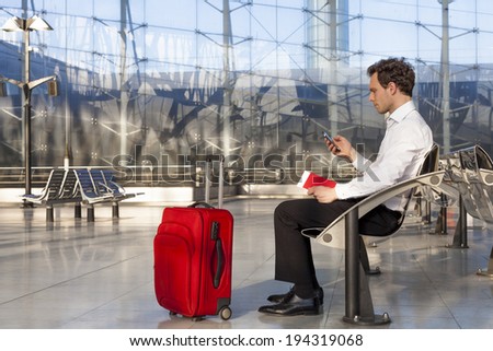 Traveling businessman waiting at lounge with smartphone and luggage