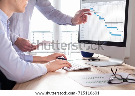 Project management team updating Gantt chart schedule or planning on computer, two business people in office 商業照片 © 